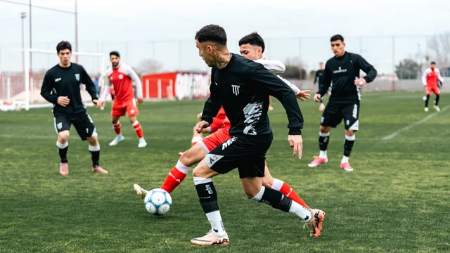 Dynamic soccer match with players in black and red jerseys engaged in a game on a green field. Choosing between a team, athlete and competition