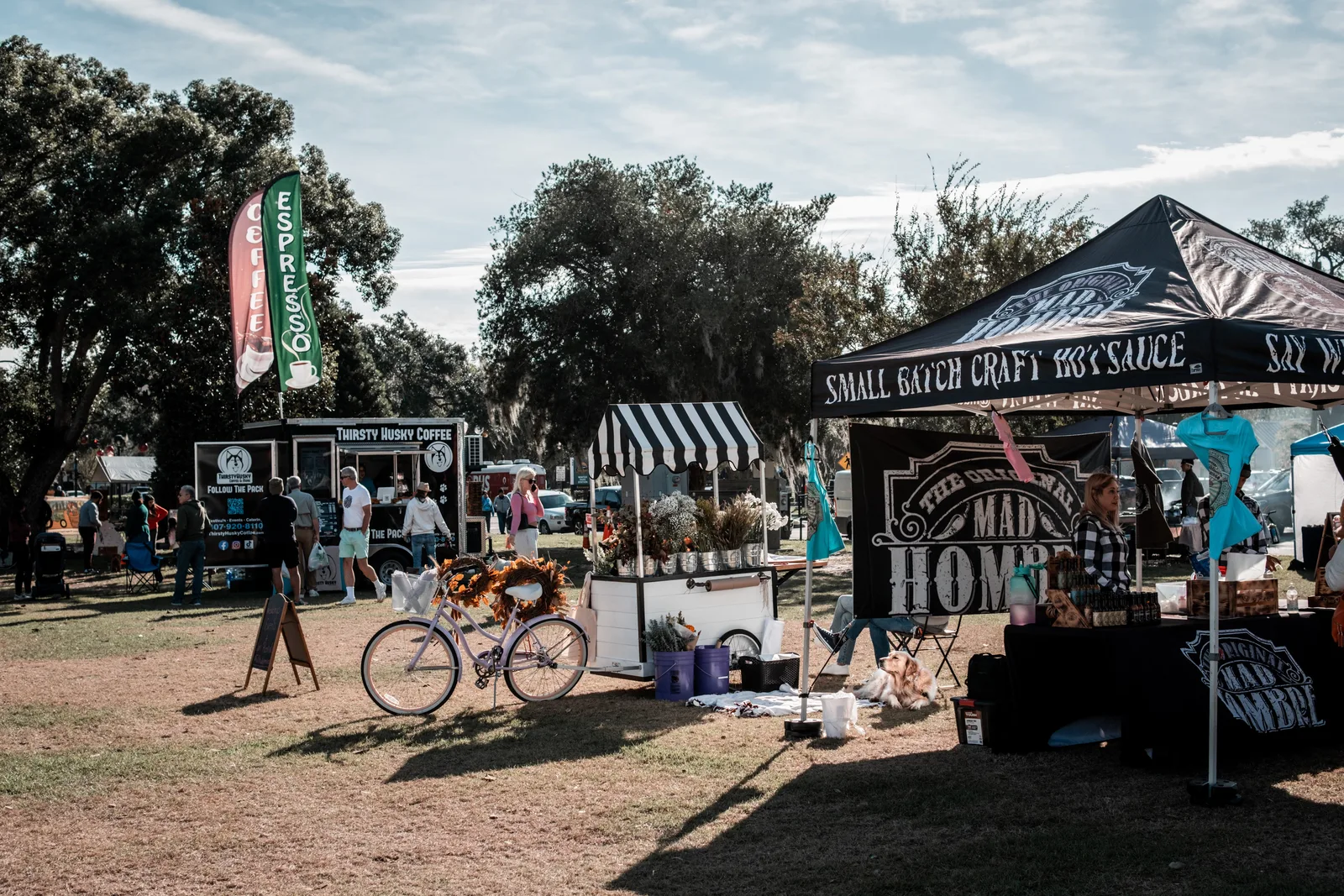 Explore a lively outdoor market scene with food stalls, shoppers, and colorful tents in a sunny park.
