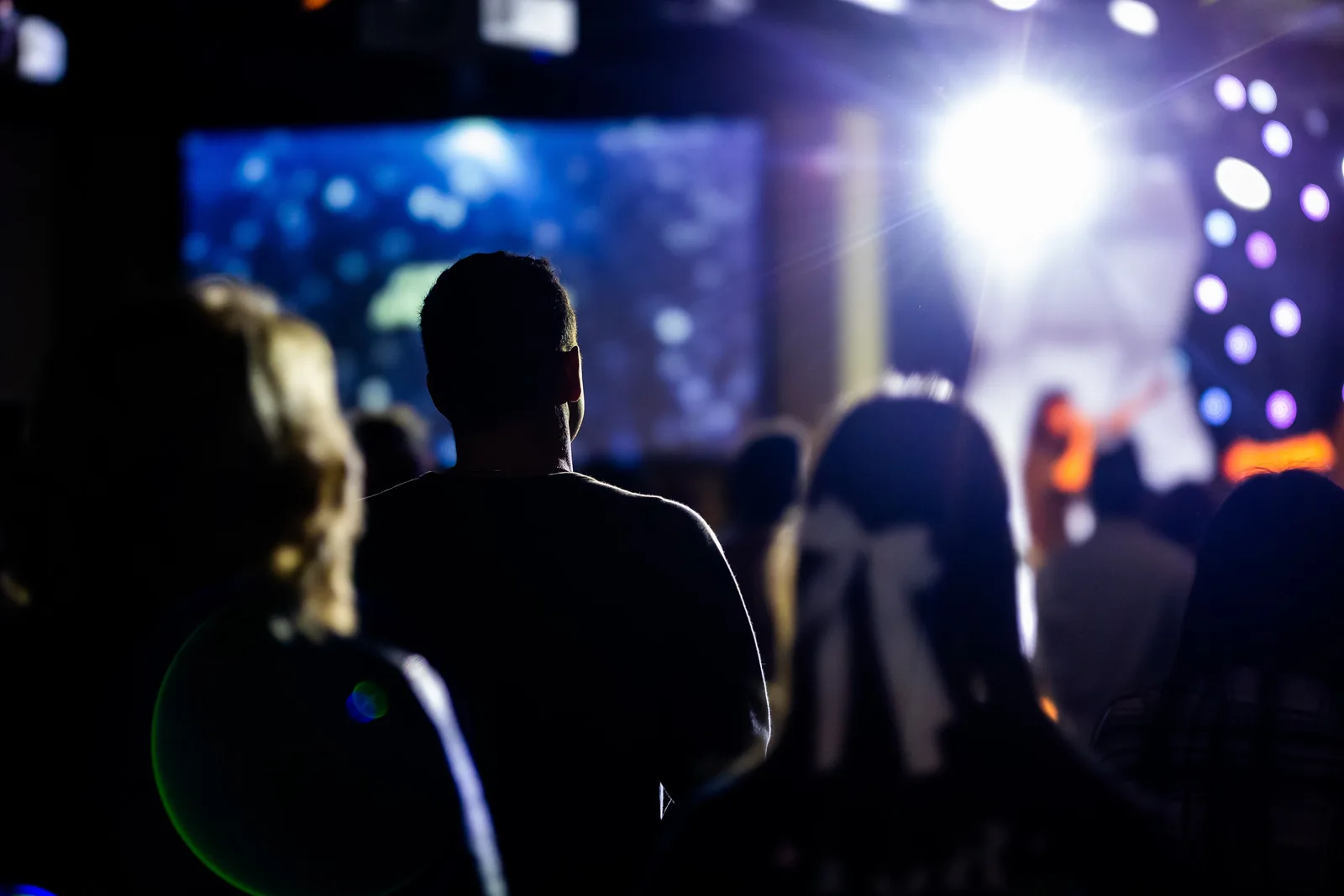 A blurred scene capturing silhouettes of people watching a live event with vibrant stage lighting.